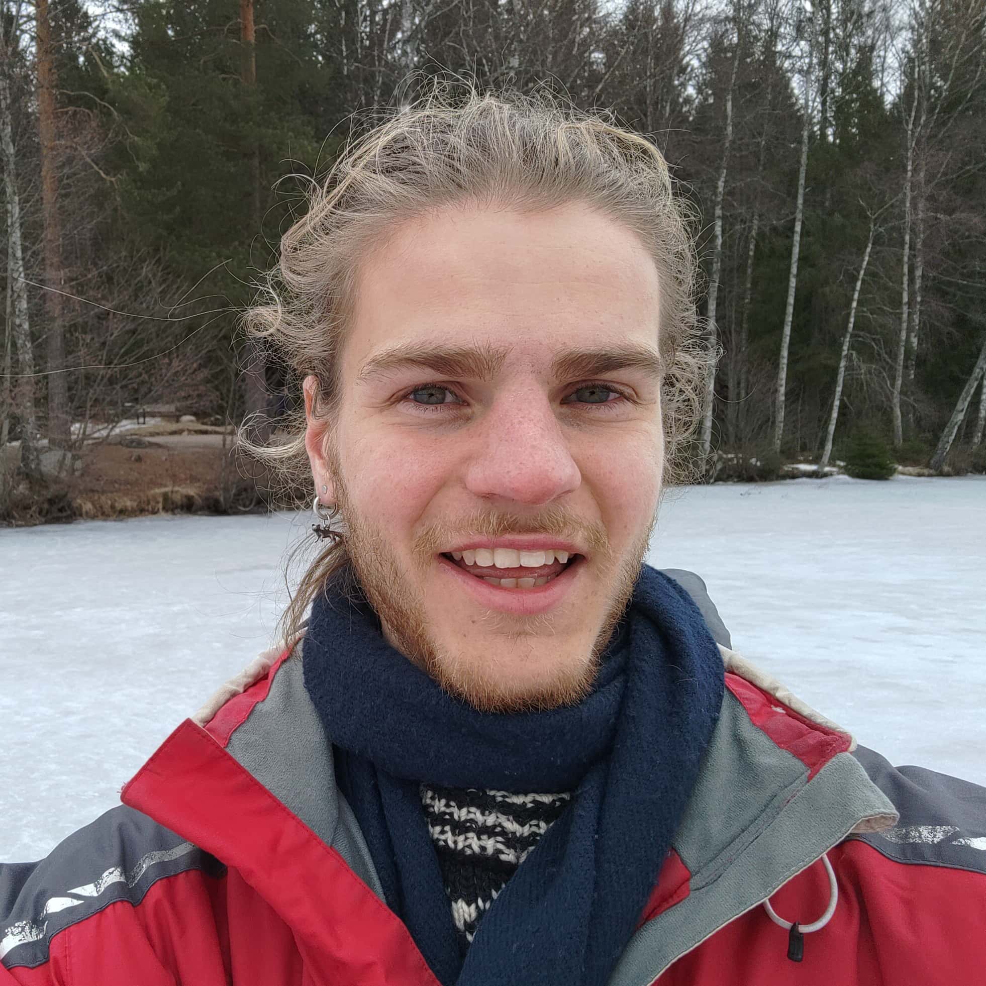 Outdoors winter selfie of a young man smiling in front of a frozen lake.