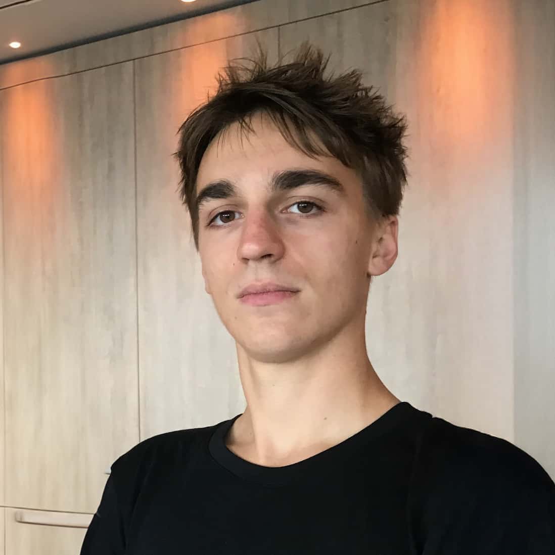 Young man posing casually indoors, wearing a black t-shirt.